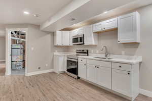 Kitchen featuring light countertops, water heater, appliances with stainless steel finishes, a sink, and light wood-type flooring