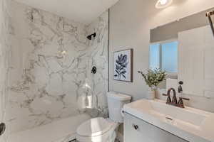 Bathroom with toilet, vanity, and a marble finish shower