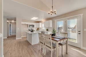 Dining area with a notable chandelier, lofted ceiling, light wood-style flooring, and baseboards