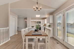 Dining room with light wood-type flooring, visible vents, vaulted ceiling, and an inviting chandelier