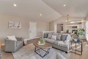 Living area featuring lofted ceiling, baseboards, light wood finished floors, and an inviting chandelier