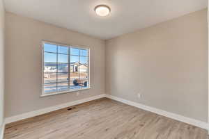 Empty room featuring light wood-style floors, visible vents, and baseboards