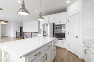 Kitchen with white cabinetry, hanging light fixtures, appliances with stainless steel finishes, light countertops, and light wood-type flooring