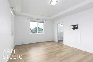 Unfurnished room with light wood-style floors, visible vents, a tray ceiling, and baseboards