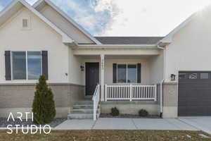 View of front of home featuring brick siding, roof with shingles, stucco siding, covered porch, and an attached garage