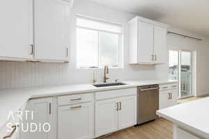 Kitchen featuring backsplash, light wood-style floors, white cabinetry, a sink, and dishwasher