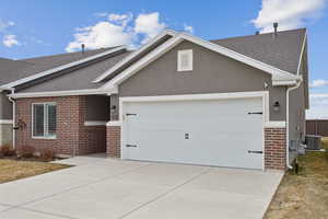 Ranch-style home with an attached garage, cooling unit, brick siding, a shingled roof, and concrete driveway