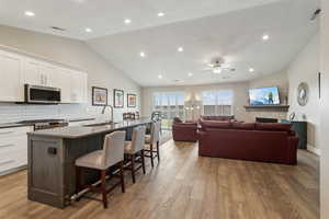 Kitchen with stainless steel microwave, a kitchen island with sink, white cabinets, a sink, and range