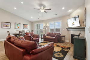 Living area with lofted ceiling, a tile fireplace, recessed lighting, visible vents, and light wood finished floors