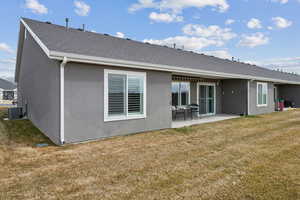 Rear view of property featuring stucco siding, a shingled roof, a lawn, a patio area, and central AC