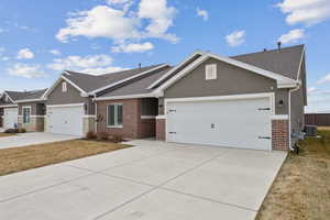 Ranch-style house featuring brick siding, central air condition unit, stucco siding, a garage, and driveway