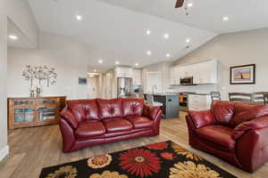 Living room featuring lofted ceiling, ceiling fan, light wood-style flooring, and recessed lighting