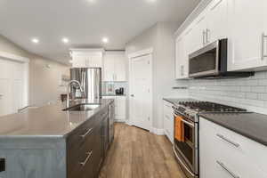 Kitchen with stainless steel appliances, light wood-type flooring, white cabinetry, a sink, and recessed lighting