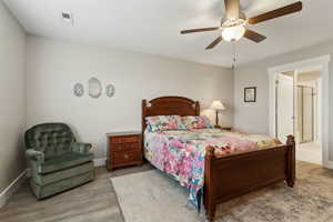 Bedroom featuring a ceiling fan, visible vents, baseboards, and wood finished floors