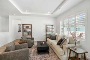 Living area with a tray ceiling, recessed lighting, wood finished floors, and baseboards