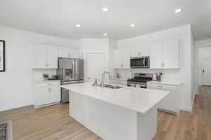 Kitchen with stainless steel appliances, an island with sink, a sink, and light countertops
