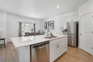 Kitchen with stainless steel appliances, a sink, white cabinets, light countertops, and a center island with sink