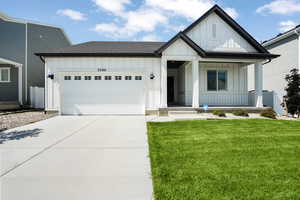 Modern farmhouse style home featuring concrete driveway, covered porch, an attached garage, board and batten siding, and a front lawn