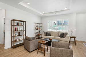 Living area with a textured ceiling, recessed lighting, baseboards, light wood-style floors, and a tray ceiling