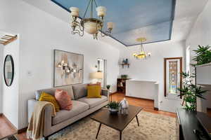 Living room with baseboards, a tray ceiling, a chandelier, and wood finished floors