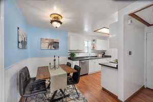 Kitchen featuring dark countertops, light wood finished floors, white cabinetry, and stainless steel dishwasher