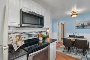 Kitchen featuring white cabinets, dark countertops, stainless steel appliances, and wainscoting