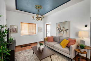 Living room featuring wood finished floors, visible vents, baseboards, a tray ceiling, and an inviting chandelier