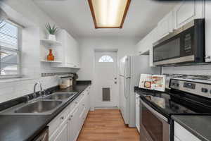 Kitchen featuring open shelves, appliances with stainless steel finishes, a sink, and white cabinetry