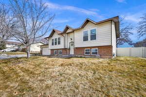 Bi-level home featuring a garage, brick siding, a front yard, and fence