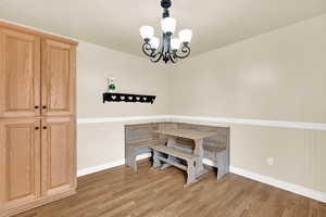 Dining space with light wood-type flooring, a wainscoted wall, baseboards, and an inviting chandelier