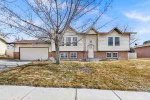 Raised ranch featuring a garage, brick siding, fence, driveway, and a chimney