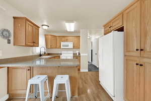 Kitchen featuring a peninsula, white appliances, a sink, light wood-style floors, and light countertops