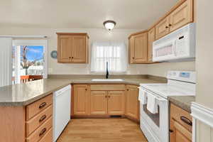 Kitchen with light wood-style flooring, a peninsula, white appliances, a sink, and light brown cabinetry