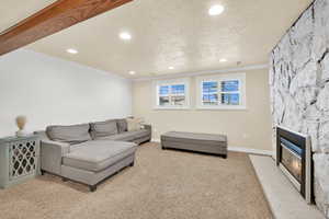 Carpeted living area with recessed lighting, ornamental molding, a stone fireplace, a textured ceiling, and baseboards