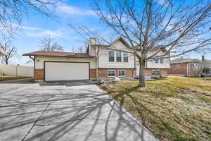 View of front of house with an attached garage, brick siding, fence, driveway, and a chimney