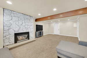 Living room with a textured ceiling, a fireplace, baseboards, beamed ceiling, and carpet