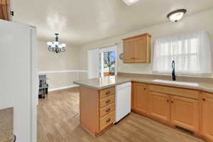 Kitchen with visible vents, light wood-style floors, a sink, white appliances, and a peninsula