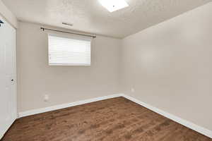 Bedroom with dark wood-style floors, baseboards, visible vents, and a textured ceiling