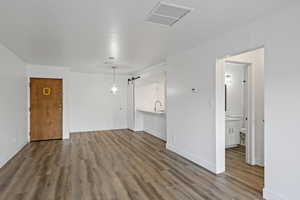 Empty room with baseboards, a barn door, visible vents, and wood finished floors