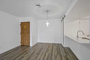 Unfurnished dining area with visible vents, a barn door, a sink, wood finished floors, and baseboards