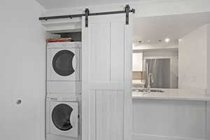 Washroom featuring laundry area, a barn door, a sink, and stacked washer and clothes dryer