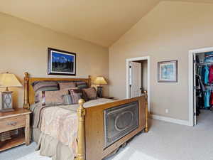 Bedroom with a walk in closet, a closet, light colored carpet, high vaulted ceiling, and baseboards