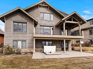 Rear view of property with stone siding, a yard, a patio area, and a balcony