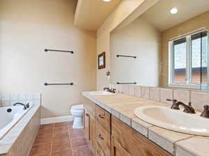 Bathroom featuring a relaxing tiled tub, a sink, toilet, and tile patterned floors