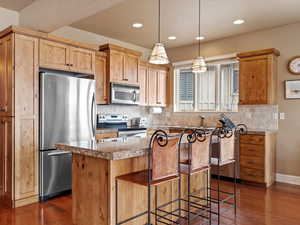 Kitchen with backsplash, a kitchen island, stainless steel appliances, and dark wood-style flooring