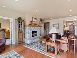 Living room featuring recessed lighting, a stone fireplace, an inviting chandelier, and wood finished floors