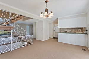 Kitchen featuring white appliances, visible vents, dark countertops, crown molding, and carpet floors