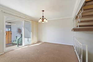 Carpeted empty room featuring baseboards, stairs, ornamental molding, and a notable chandelier
