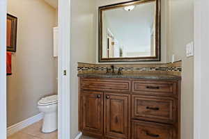 Bathroom with toilet, vanity, backsplash, and tile patterned floors