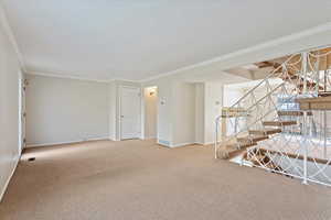 Carpeted empty room featuring baseboards, visible vents, stairway, and crown molding
